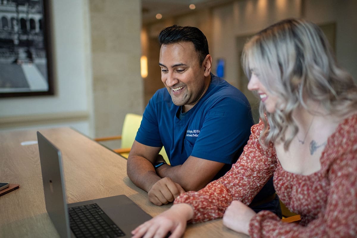 Two people smiling and working on a laptop together