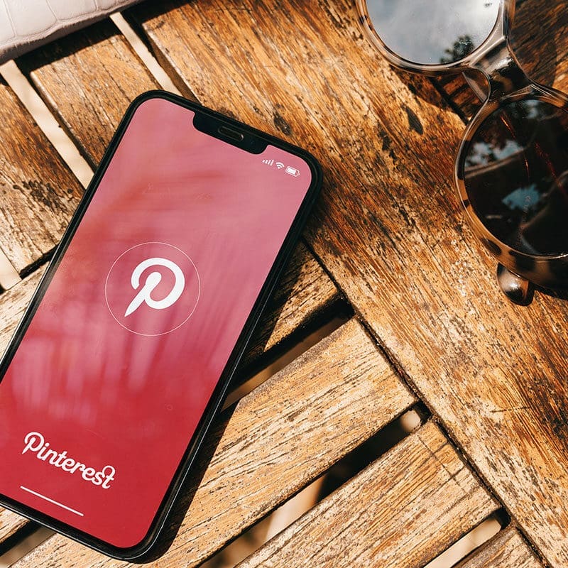 A phone on a table with the Pinterest login page, there is sunglasses next to the phone