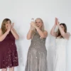 Three women celebrate with colorful confetti, smiling and clapping in front of a white wall, marking a joyful 5th birthday occasion.