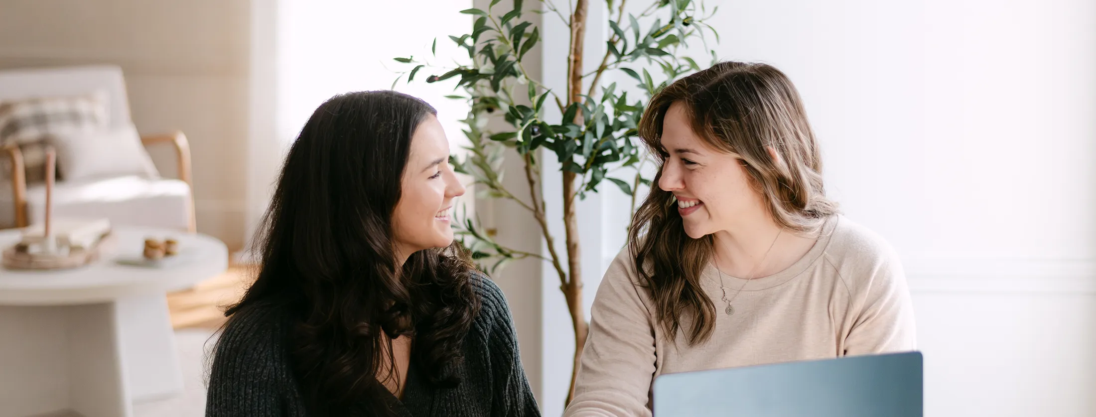 a creative professional at Don Creative Group, smiles while collaborating with a model during a planning session at a bright, modern workspace featuring natural light, greenery, and a laptop on the table.