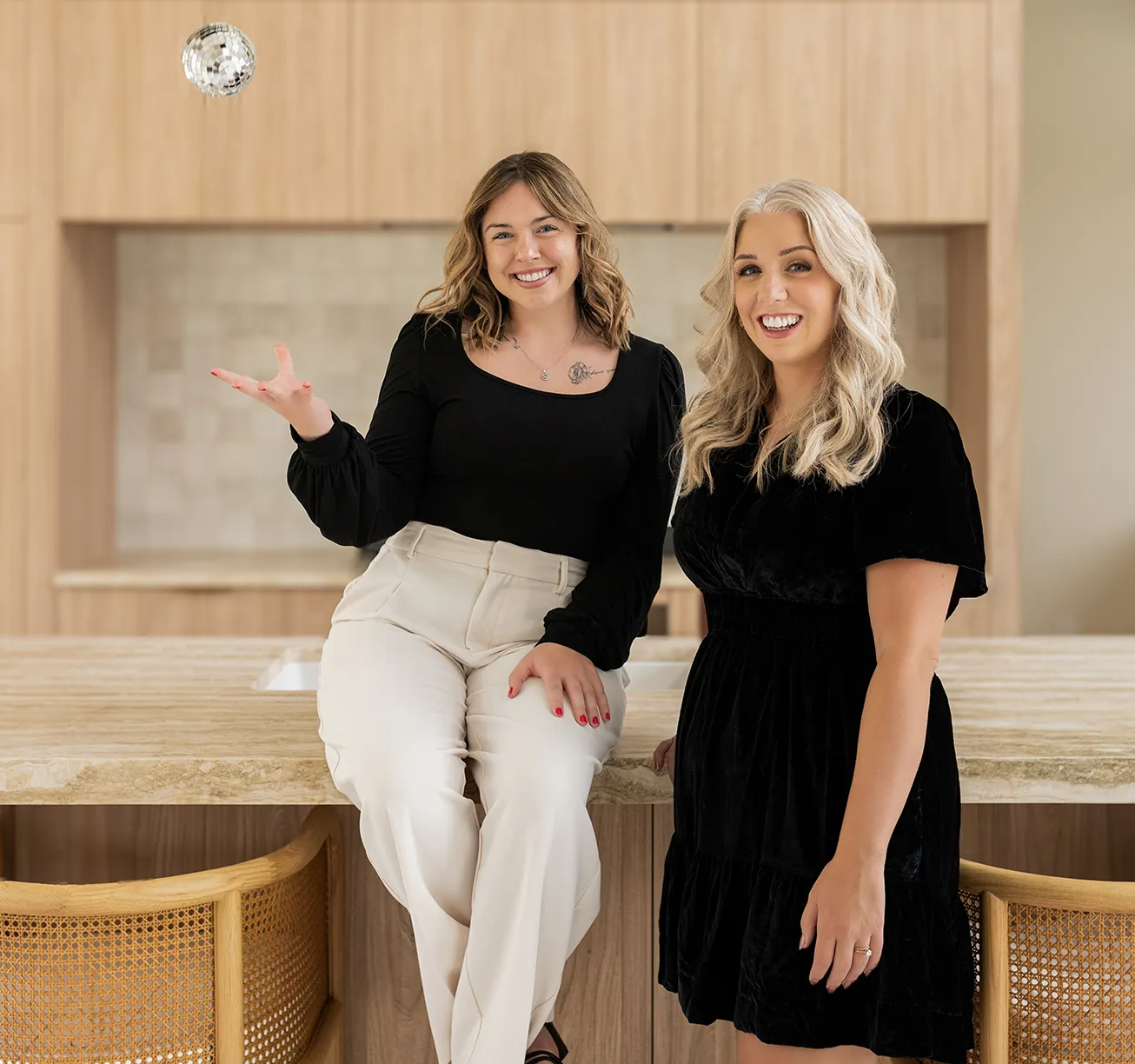 Madison and Lauren from Don Creative Group pose in a modern kitchen workspace, smiling and showcasing a playful, creative energy as Madison tosses a small disco ball.