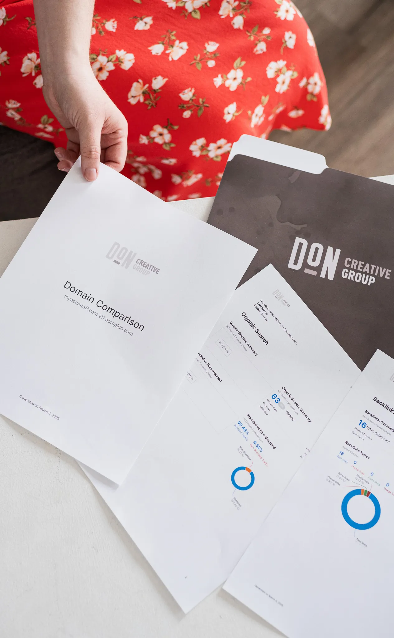 Person reviewing Don Creative Group domain comparison and SEO analytics reports placed on a table.
