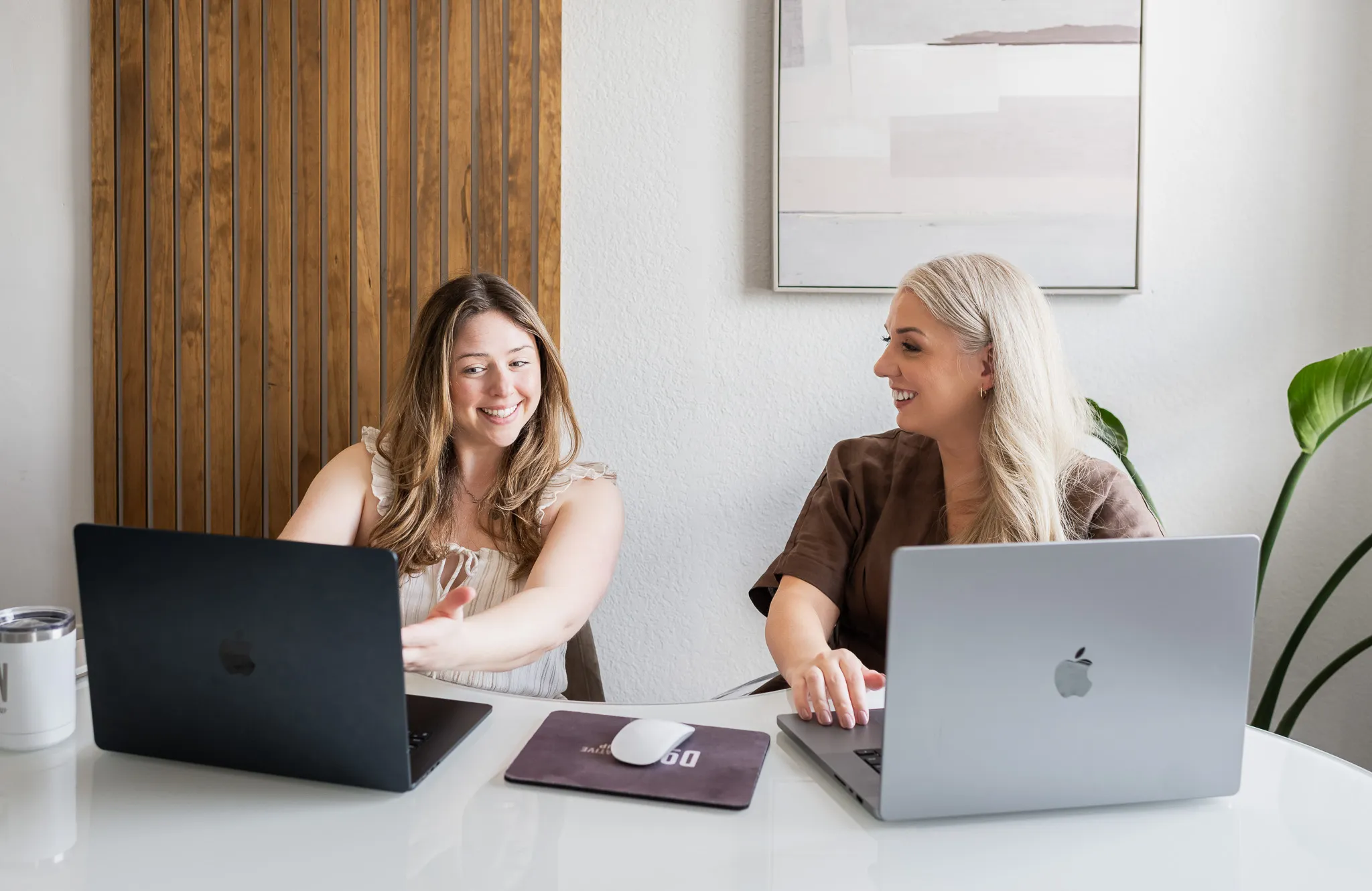 Two women working together at a desk with laptops, smiling during a collaborative meeting at Don Creative Group.