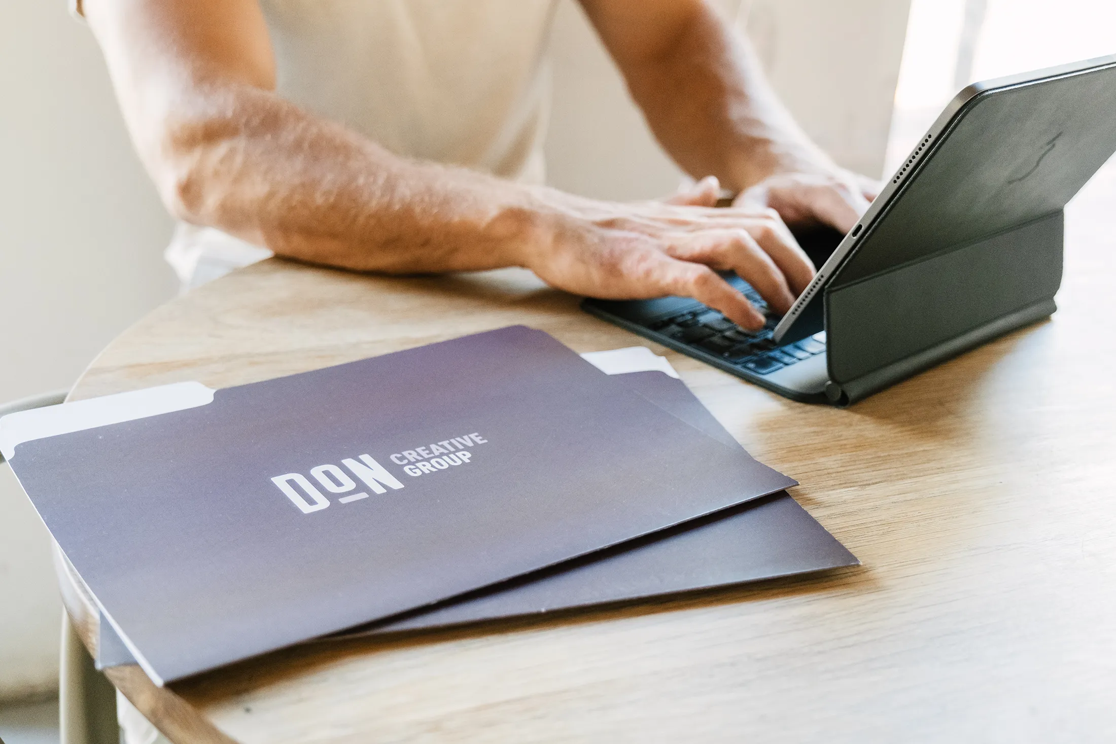 Person typing on a tablet at a desk with Don Creative Group branded folders
