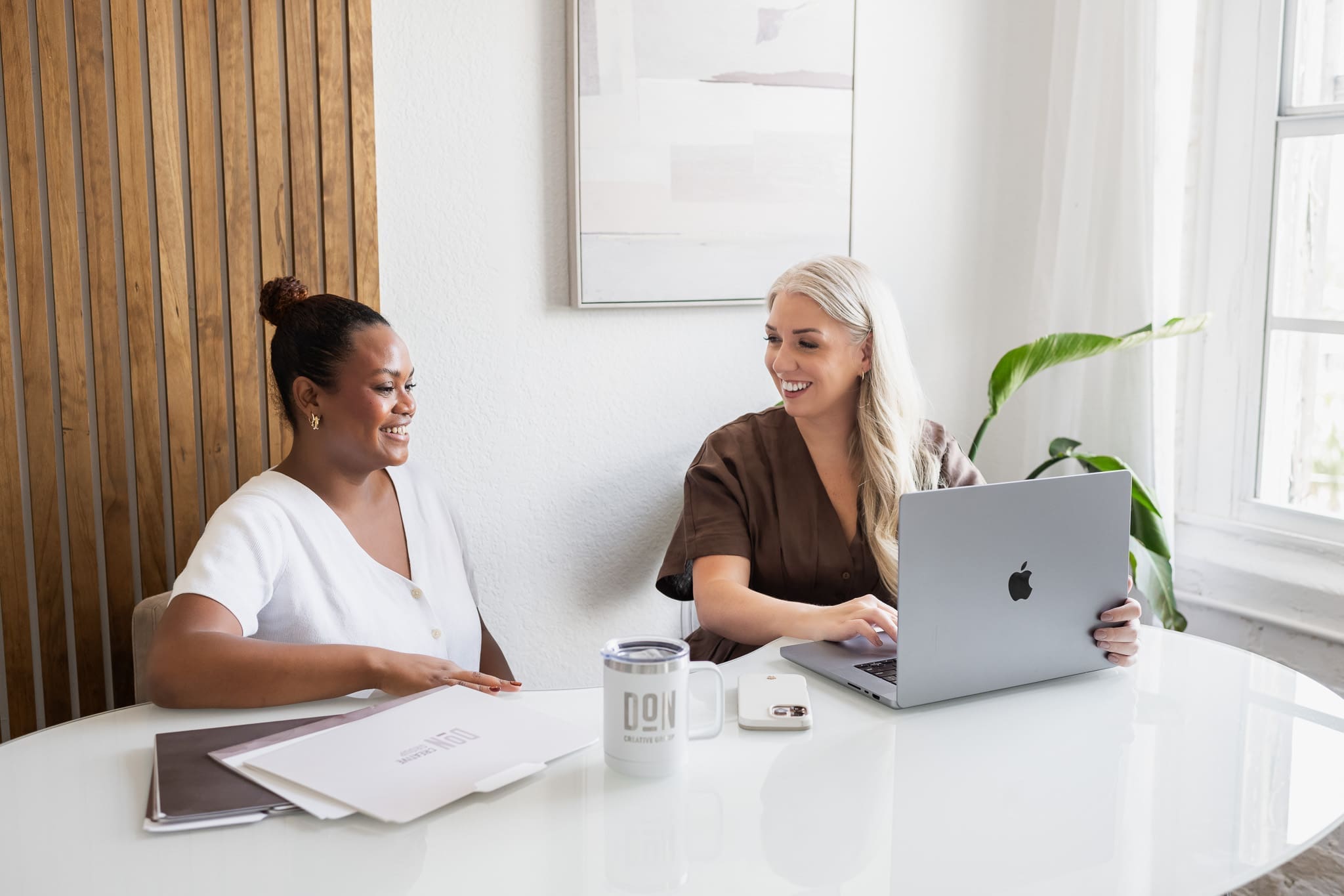 Two consultants discussing strategy at table with laptop and Don Creative Group materials