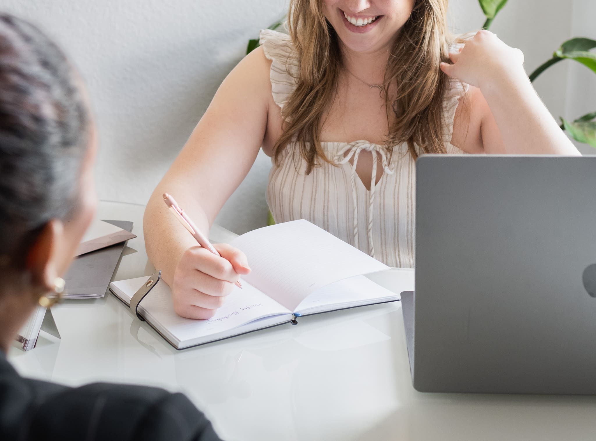 Consultant taking notes during in-person meeting with laptop open on desk