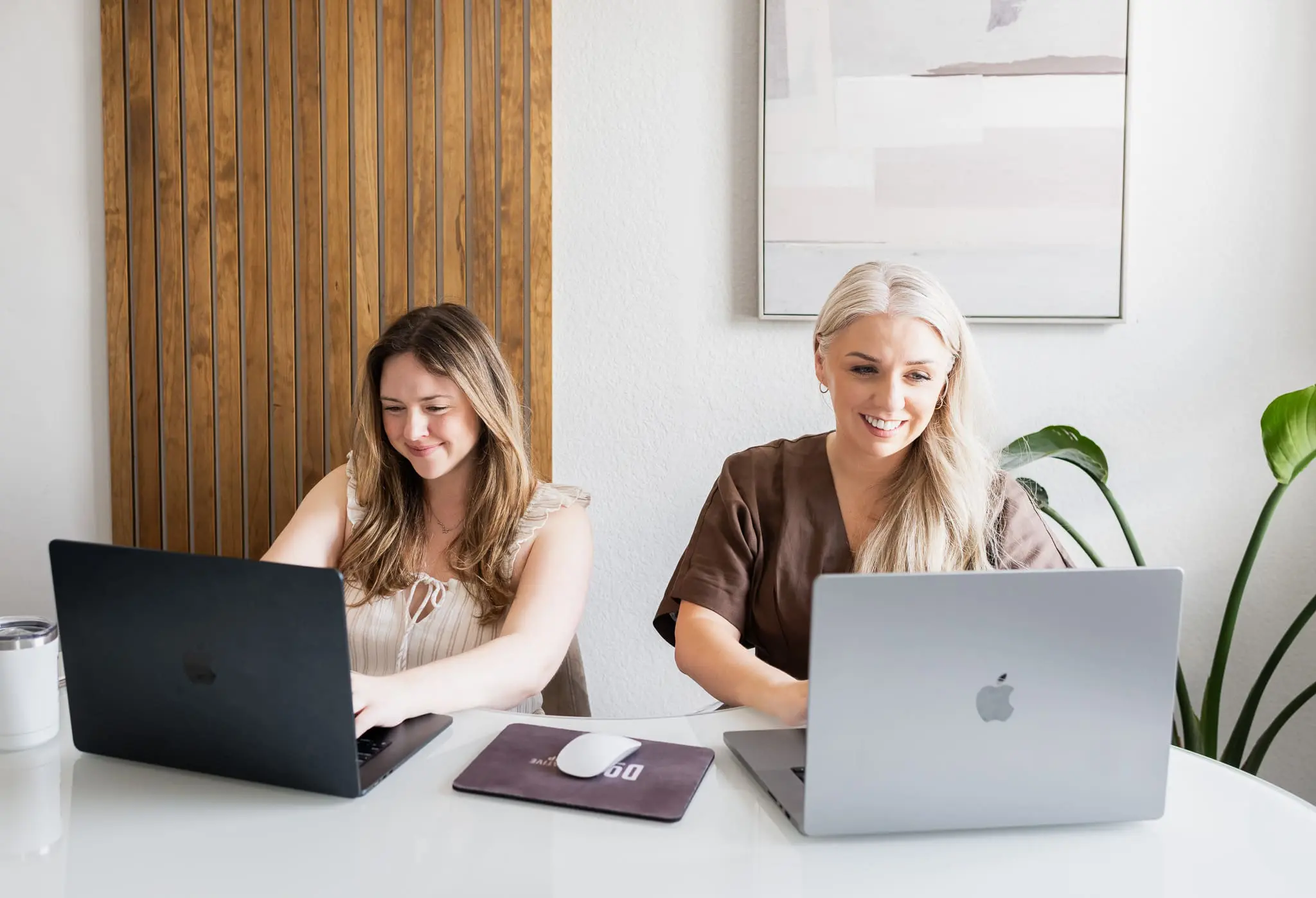 Two team members working side by side on laptops at shared desk