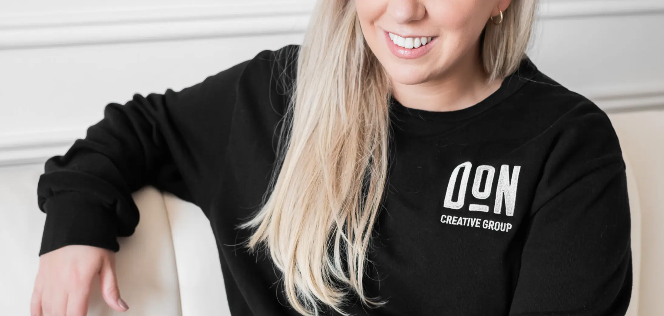 xTeam member wearing black Don Creative Group sweatshirt, seated indoors and smiling