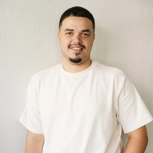 xDouglas standing against light wall smiling at camera wearing white shirt