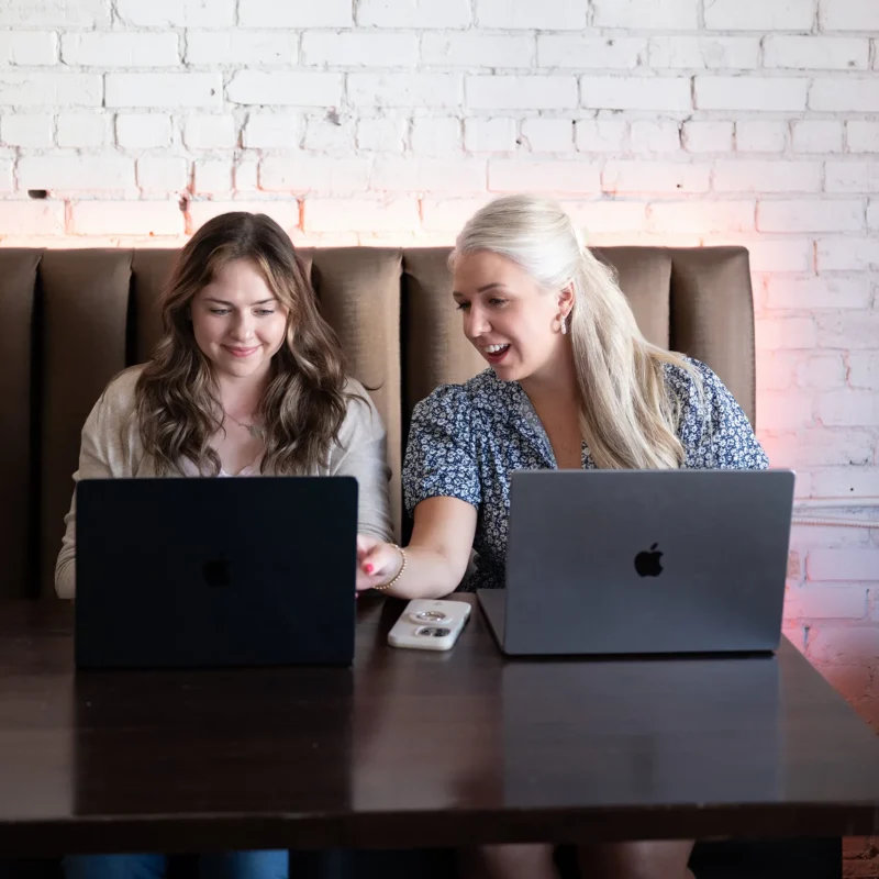 Maddie and Lauren working side by side on laptops at a shared table
