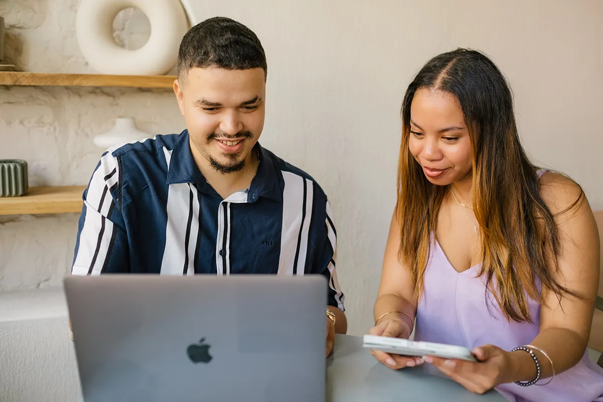 xTwo team members reviewing laptop and mobile device together at shared workspace