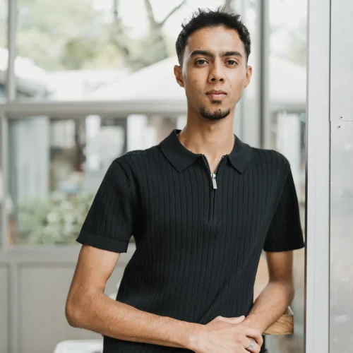 xTeam member standing indoors wearing black shirt, hands resting on wooden railing