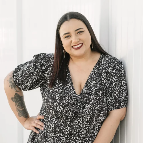 xTeam member smiling while standing against white wall wearing patterned black dress