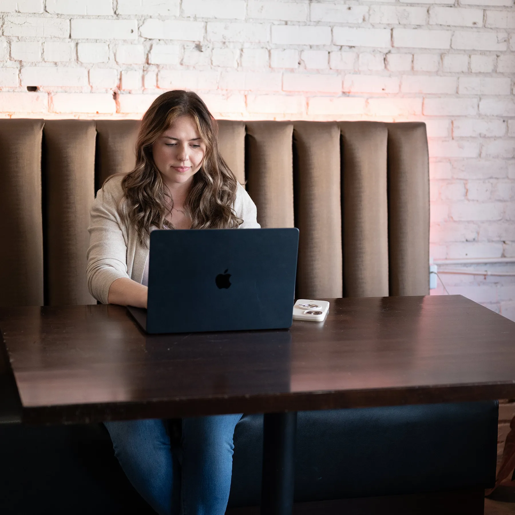 xTeam member seated at table using laptop in booth with brick wall