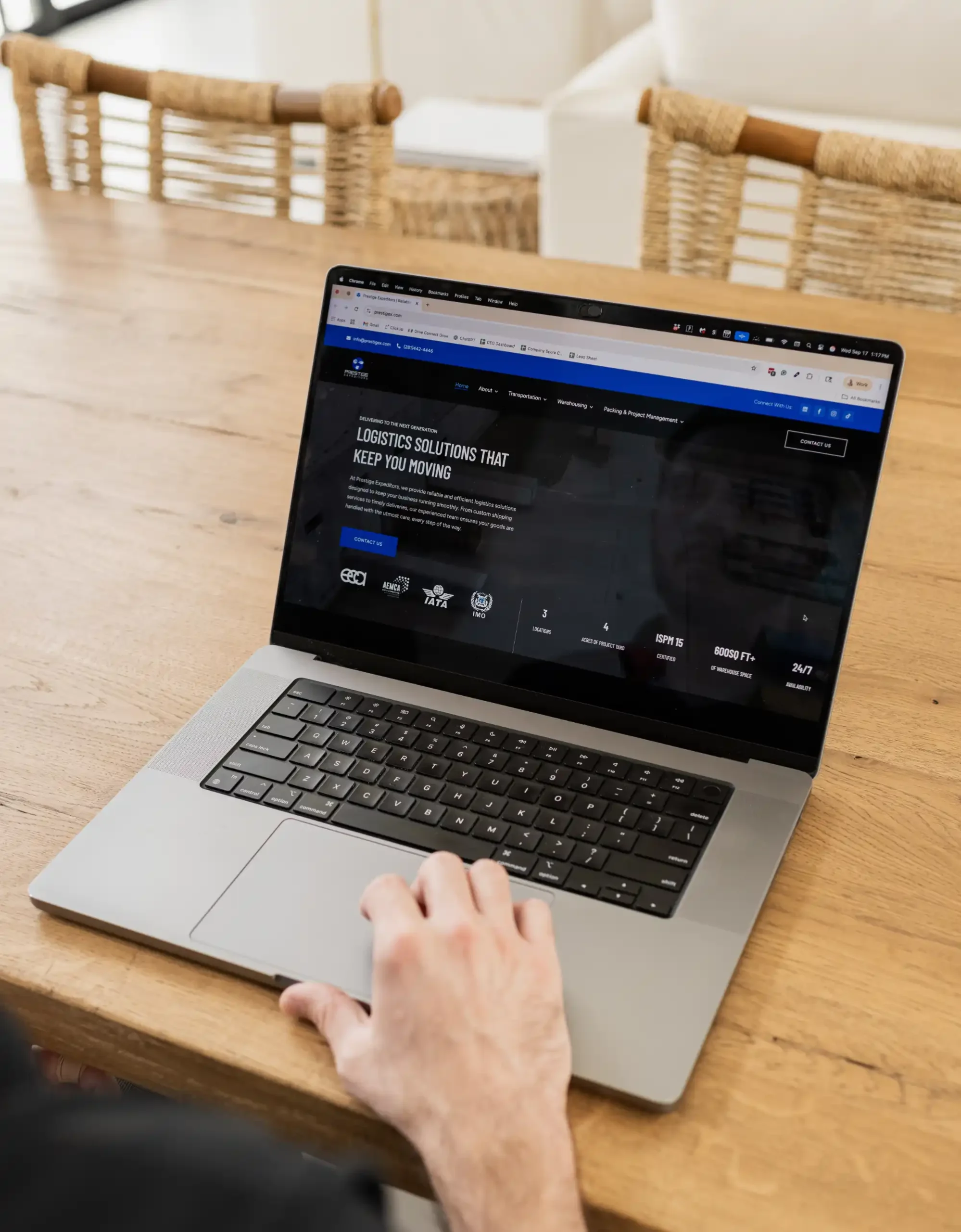 A person browses a logistics company website on a laptop placed on a wooden table in a bright home setting.